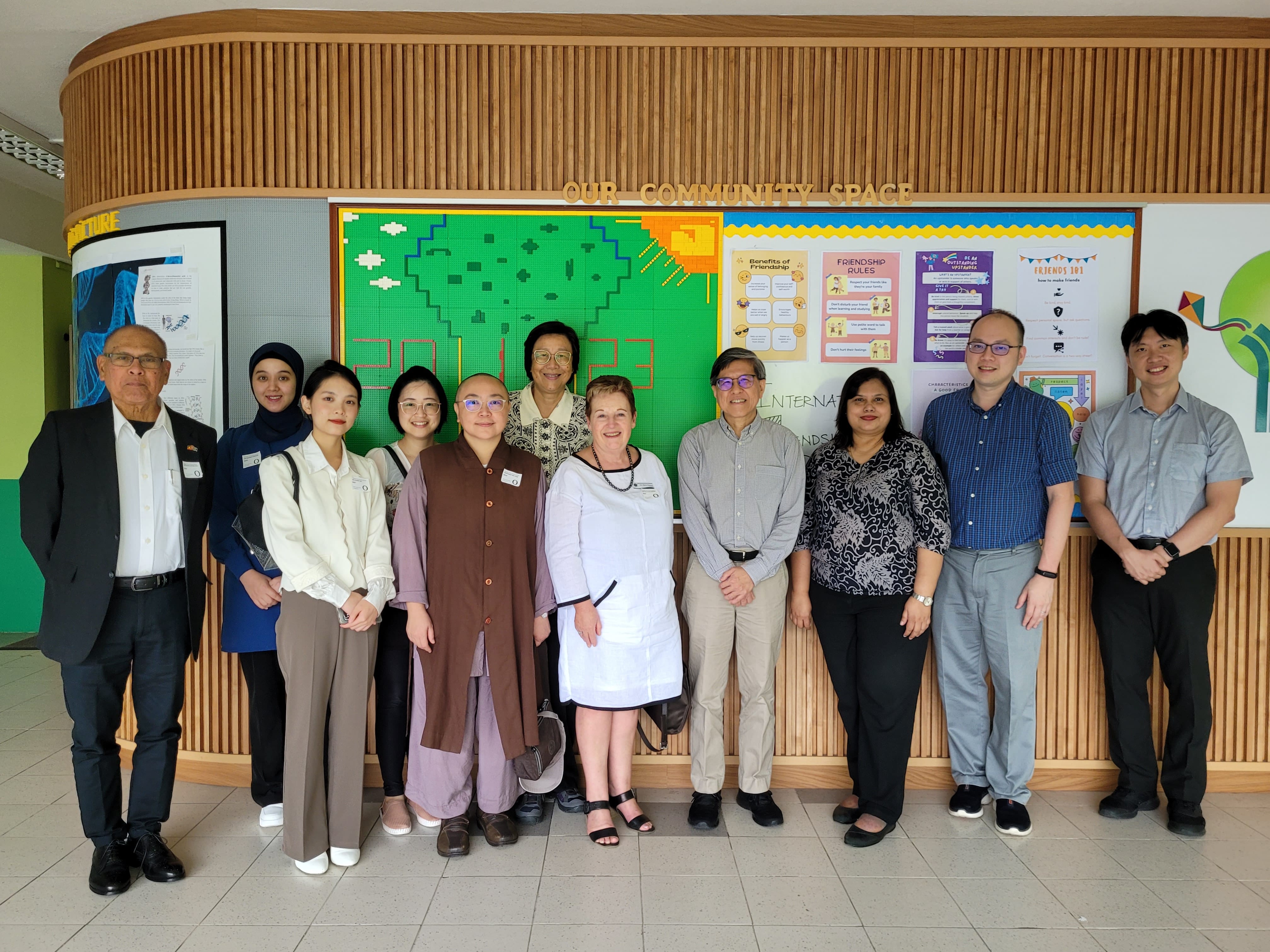 A group of eleven people posing together in front of a colorful "Our Community Space" display wall.
